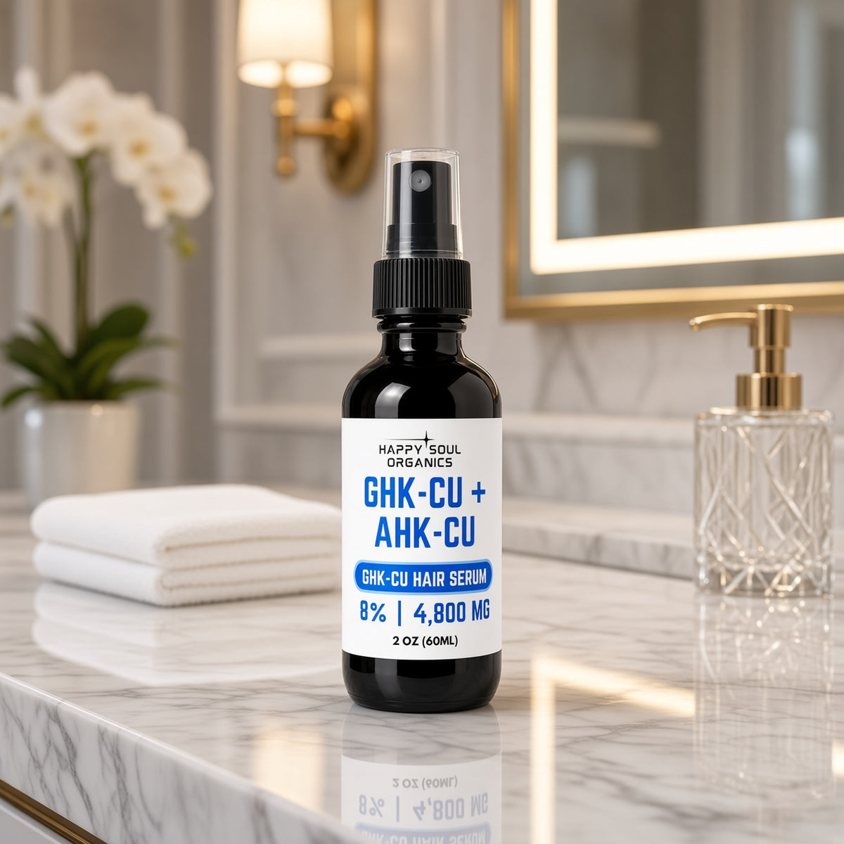 A 2 oz bottle of Happy Soul Organics GHK-CU + AHK-CU Hair Serum stands on a marble bathroom counter next to a folded white towel, with a gold-framed mirror and soap dispenser in the background.